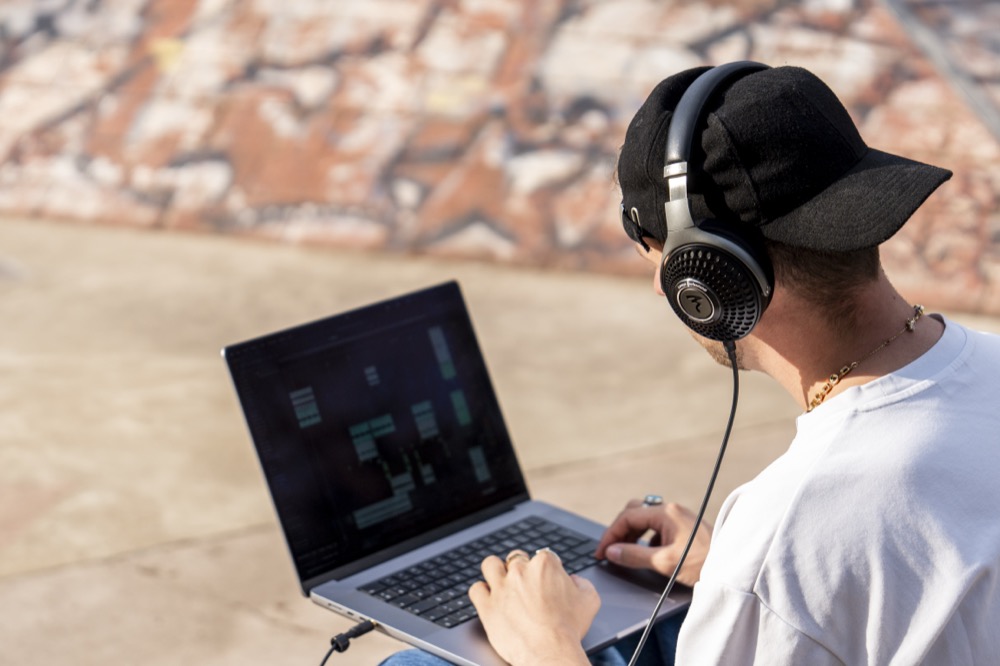 Photo of the back of a person sitting down and staring at laptop screen mixing music while wearing Focal Lensys